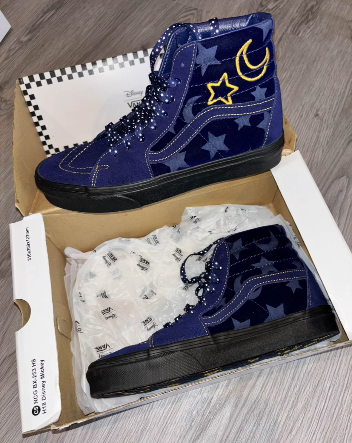 Blue shoes with star and moon design in a box on a wooden floor.